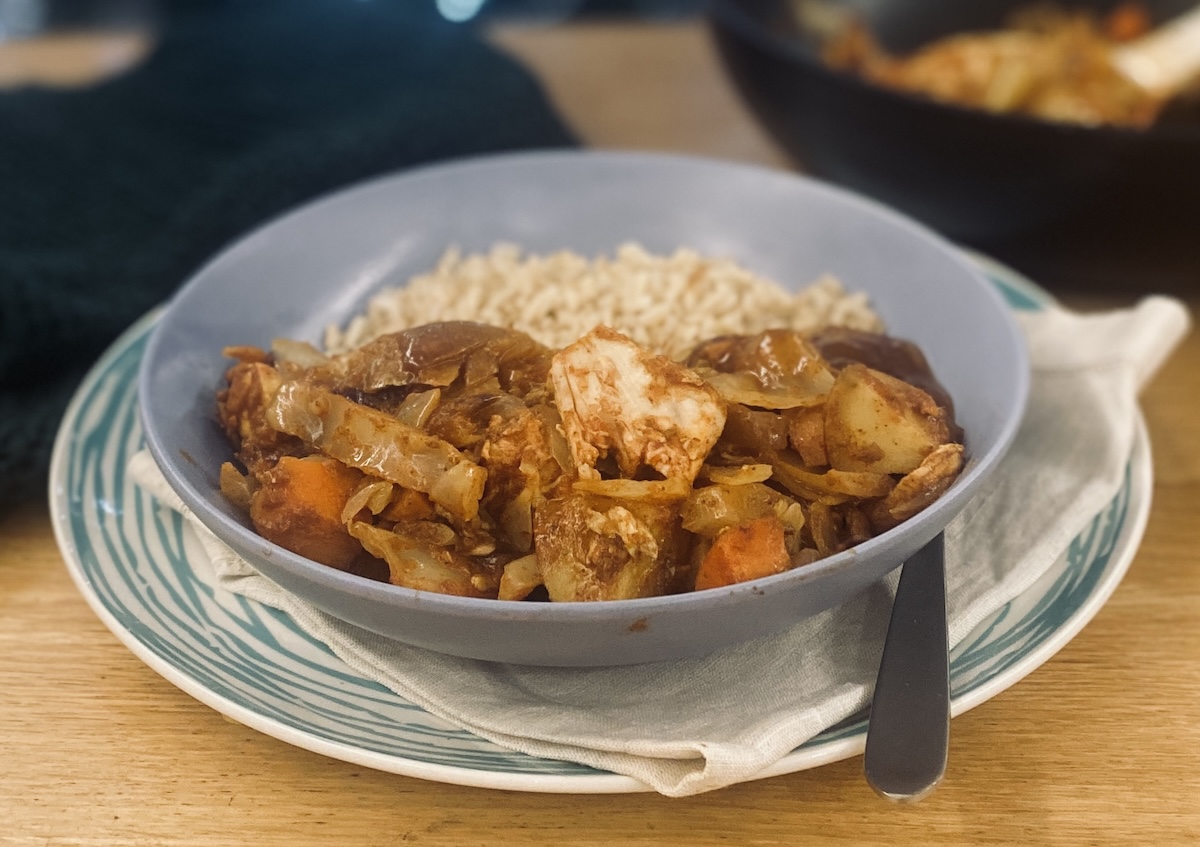 leftover chicken curry, in a blue bowl, on a blue striped plate.