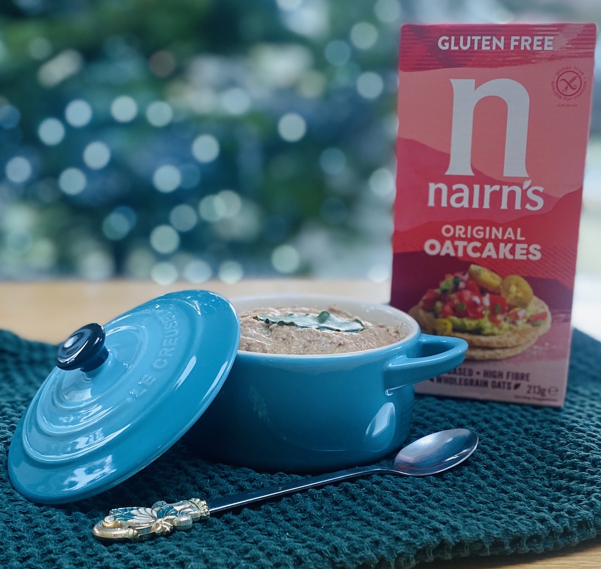 turkey liver pate in a small (250 ml) pale blue le creuset dish, on a green waffle tea-towel, with a box of oat cakes in at the background and a long handled tea spoon on the foreground