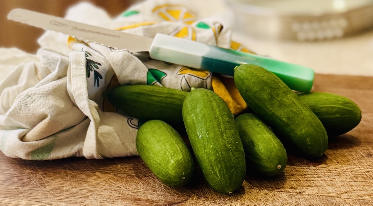 cucumber on a wooden board, with a tea-towel and a knife.