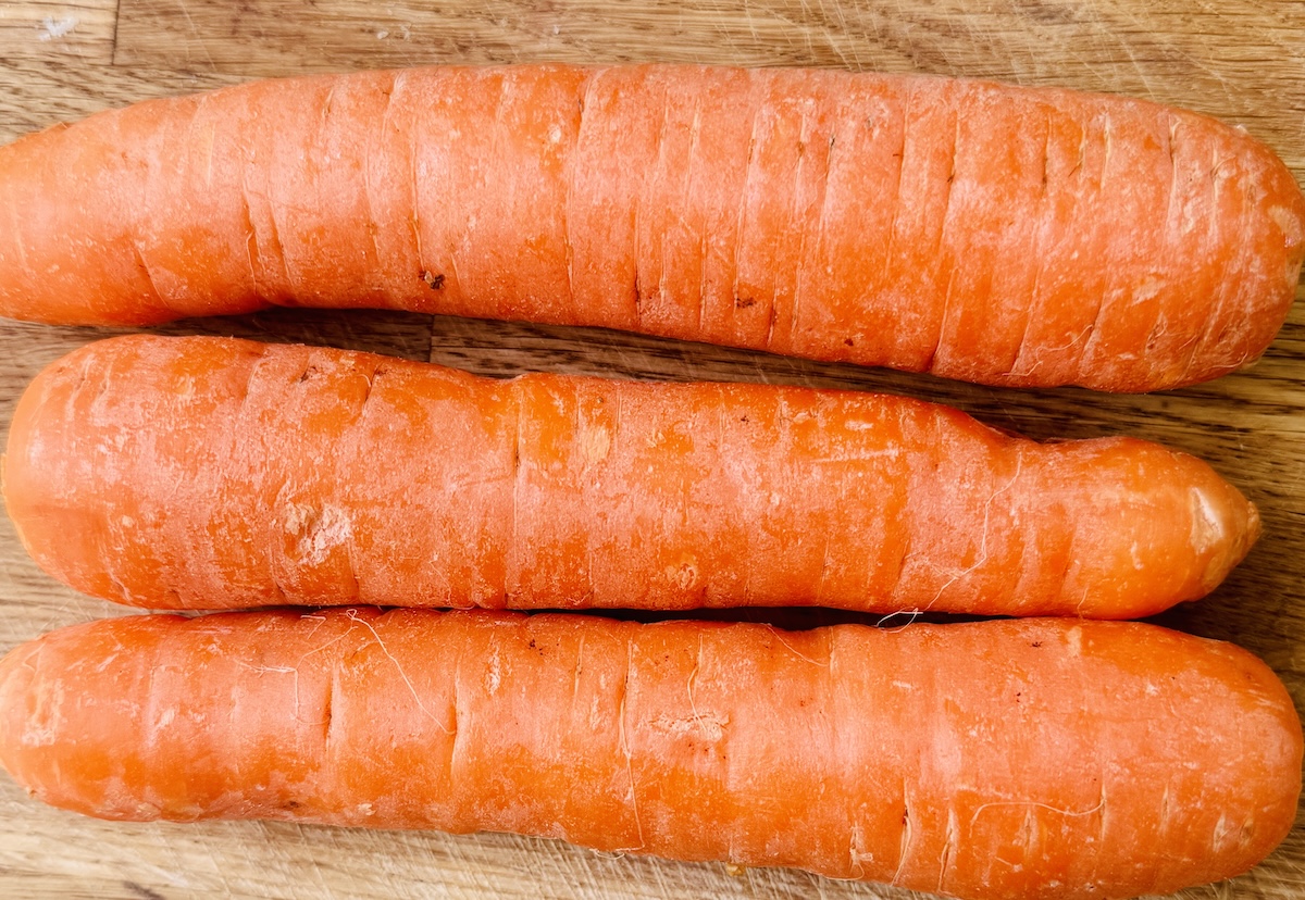 Three mature carrots on a wooden chopping board.